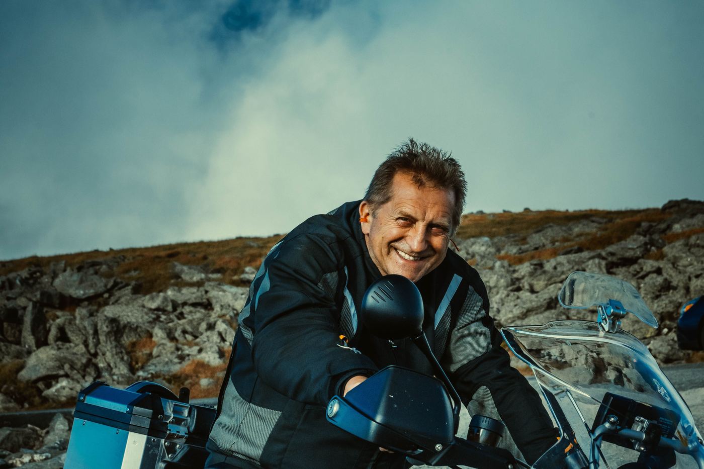 A veteran rider smiling on his adventure motorcycle in the mountains.
