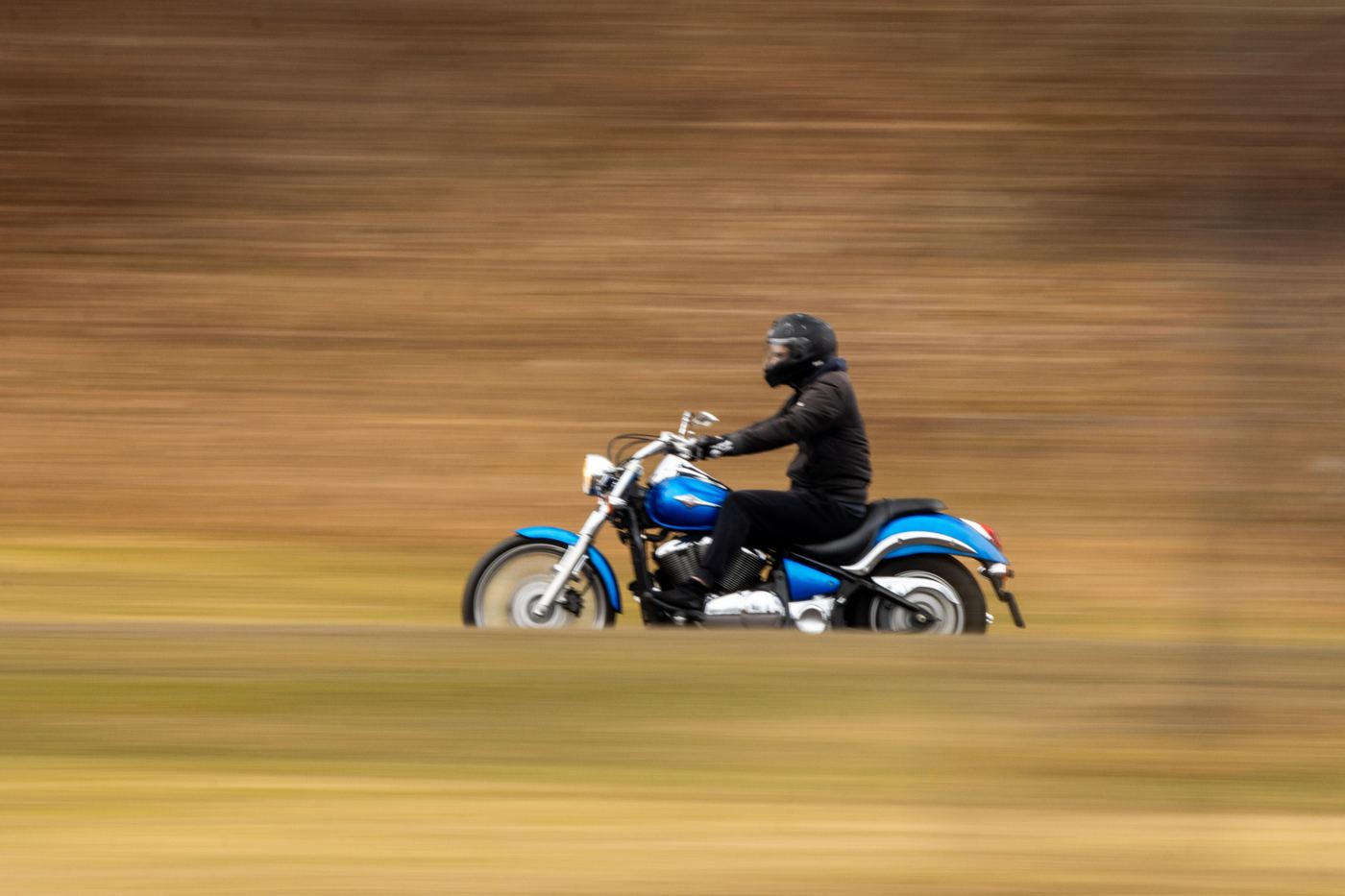 A helmeted rider at speed on a cruiser, the background blurred by motion.
