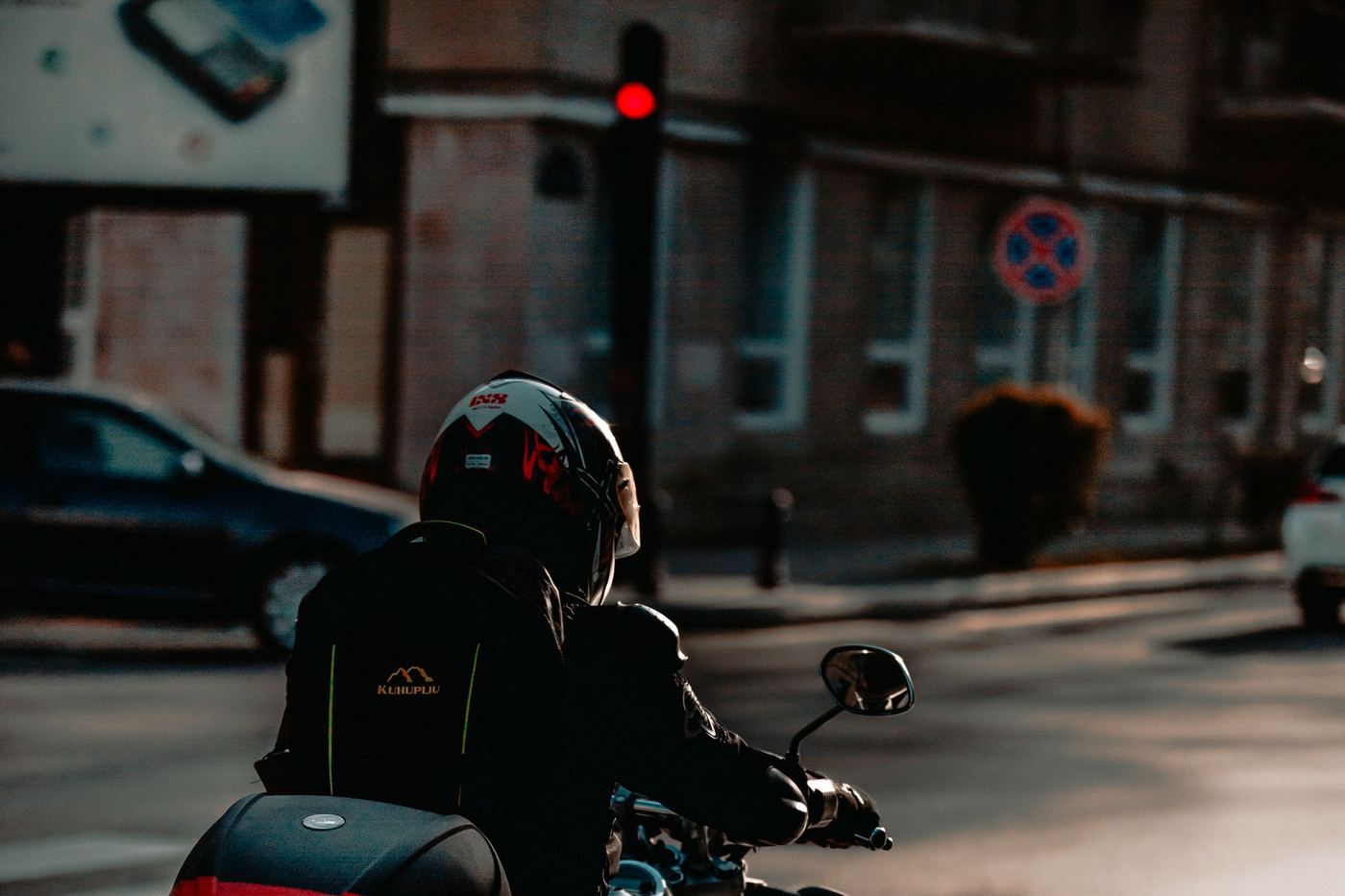 A motorcyclist waiting at a red light on an ordinary city street, seen from behind.