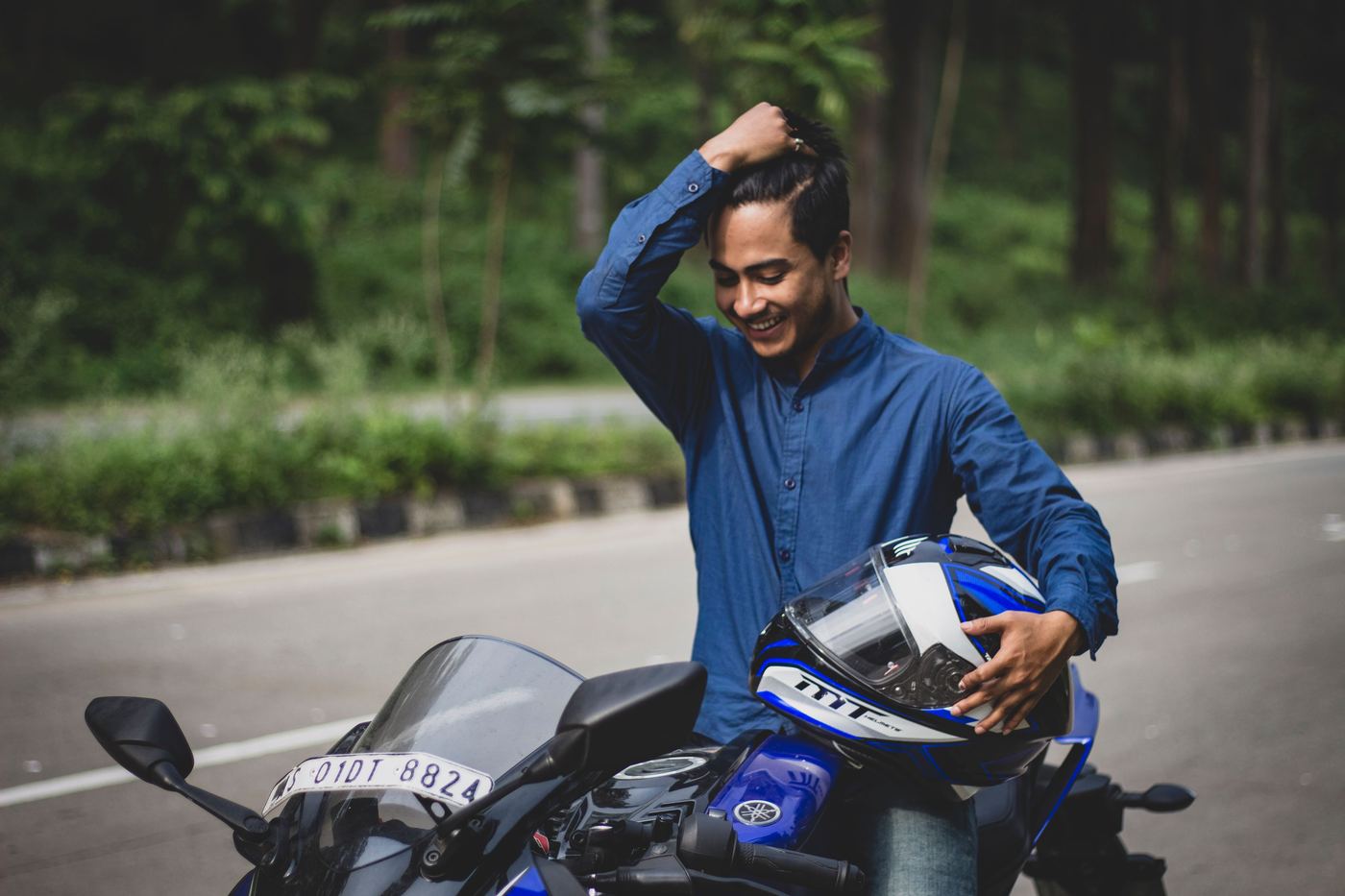A rider smiling as he lifts his helmet beside his motorcycle.